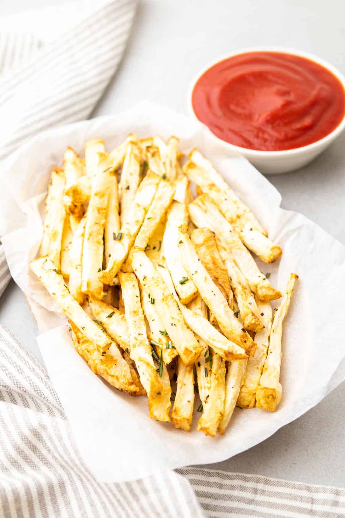 Primo piano di patate fritte di sedano in un cestino accanto a un ramekin di ketchup