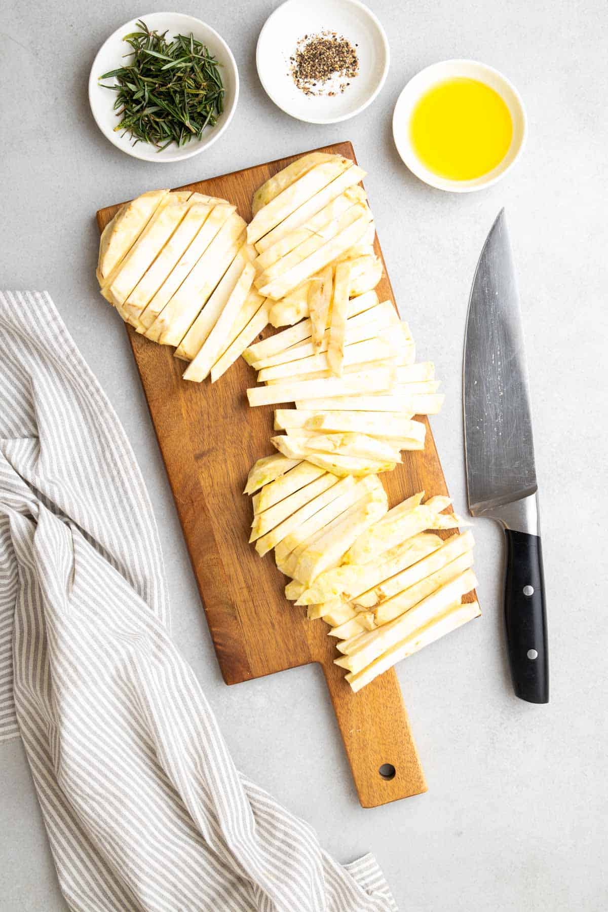 Radice di sedano tagliata a fiammiferi su un tagliere di legno accanto a stampini di altri ingredienti